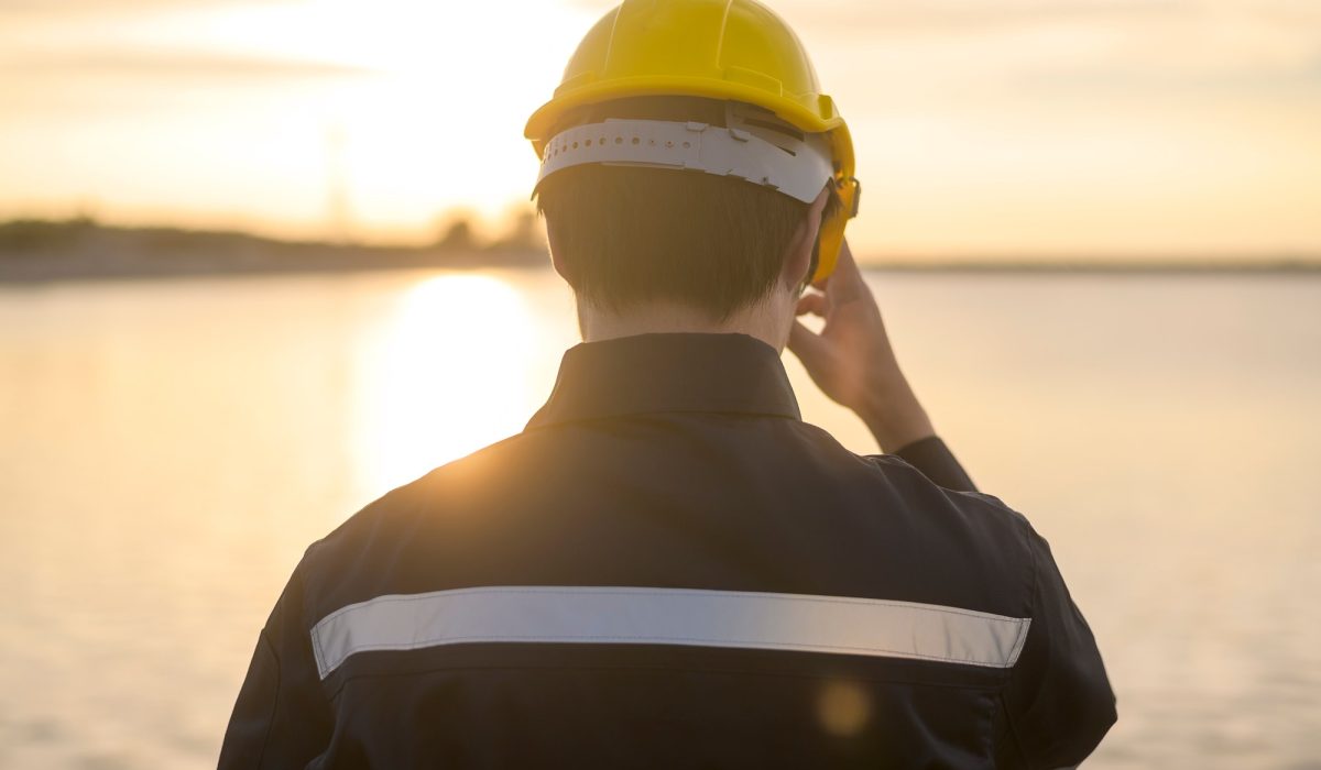 A male engineer wearing a protective helmet at sunset.